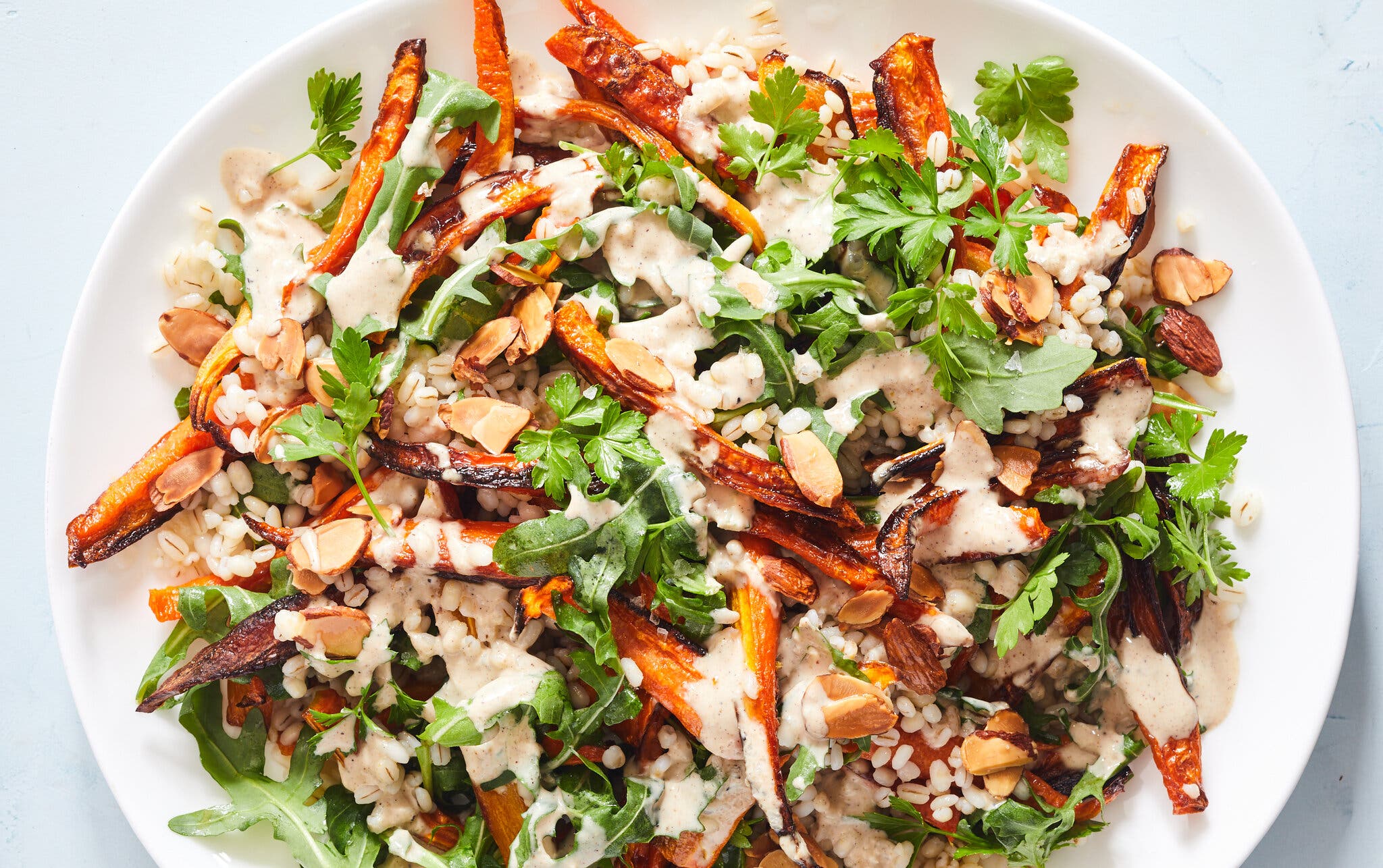 A white bowl holds grains, roasted carrots, arugula, almonds and parsley.