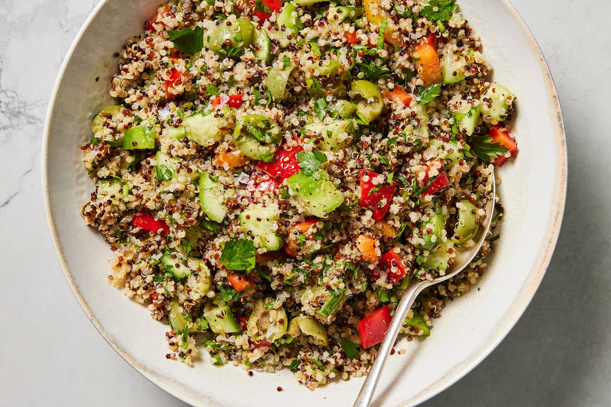 A white ceramic bowl holds quinoa salad with a spoon.