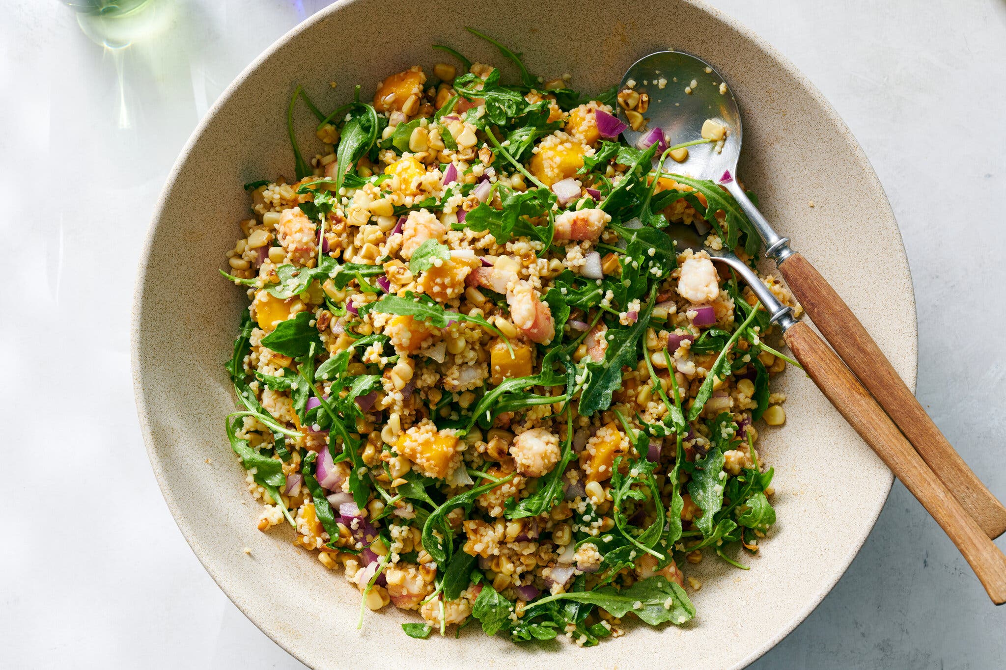 A ceramic bowl holds millet, corn, shrimp, peaches, chopped red onion and arugula.