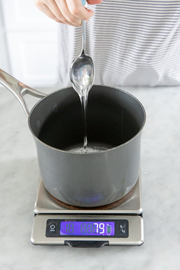 Using a scale to weigh a precise amount of glucose syrup into a saucepan.