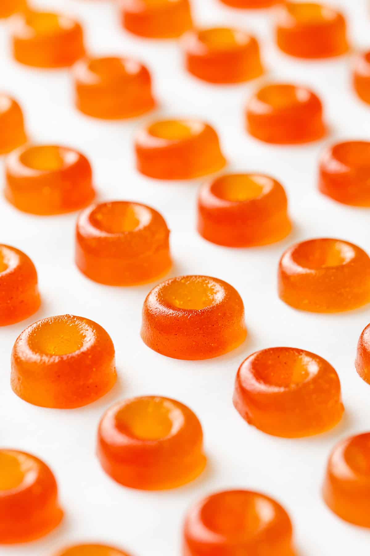 Rows of Homemade Gummy Peach Rings, with two-toned color effect, lined up on parchment paper.