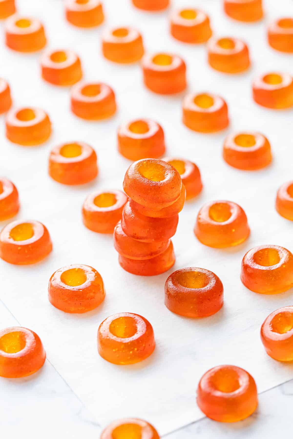 Stack of small Gummy Peach Rings with two toned orange and red color effect on parchment paper background.