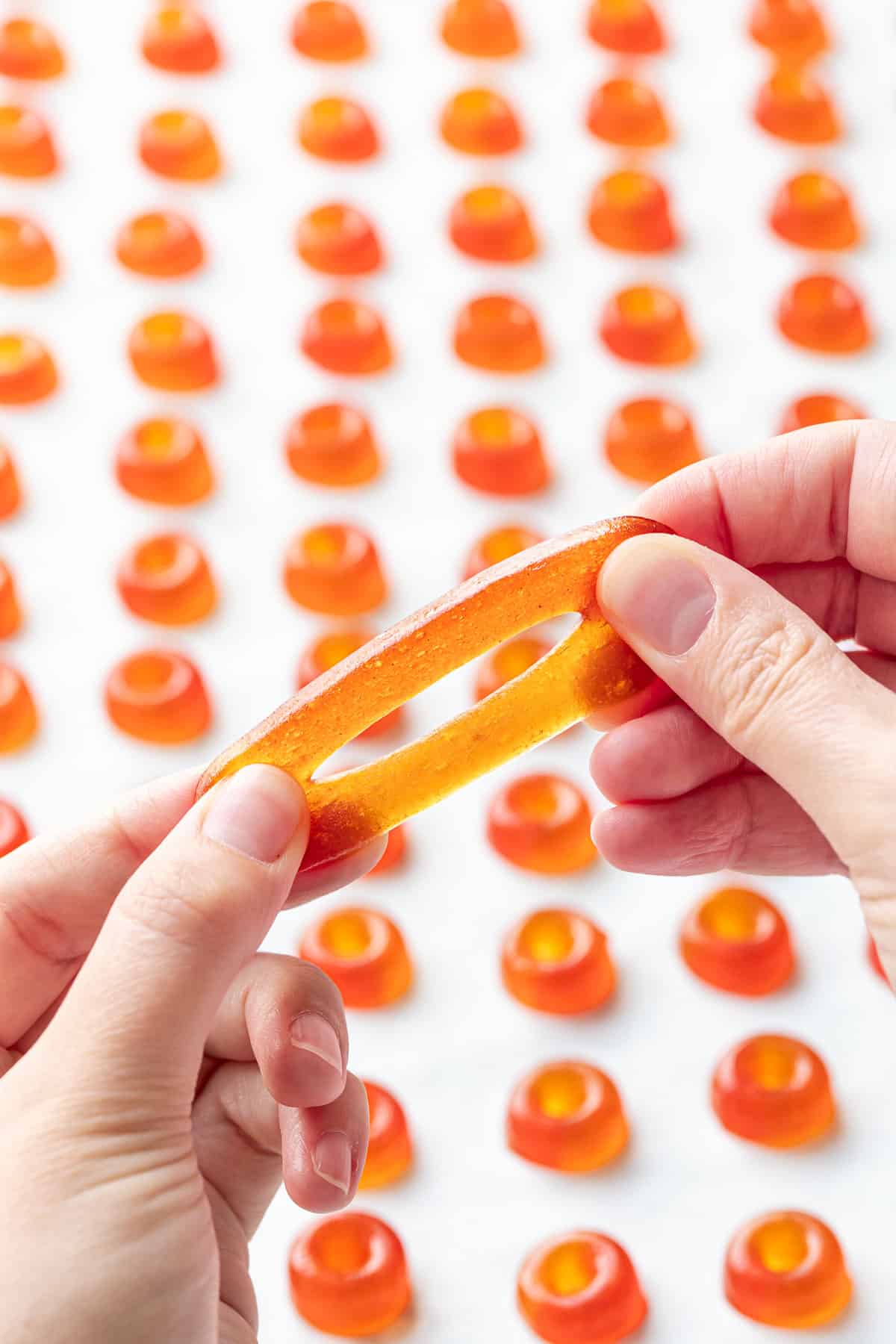 Stretching a large Homemade Gummy Peach Rings to show the bouncy, stretchy, gelatin-based texture.