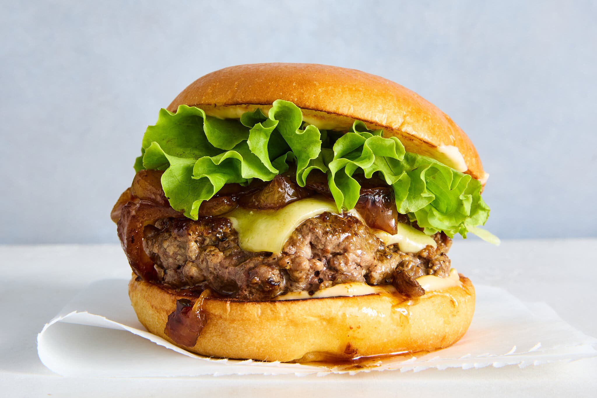 A side image of a thick burger topped with onions and lettuce.