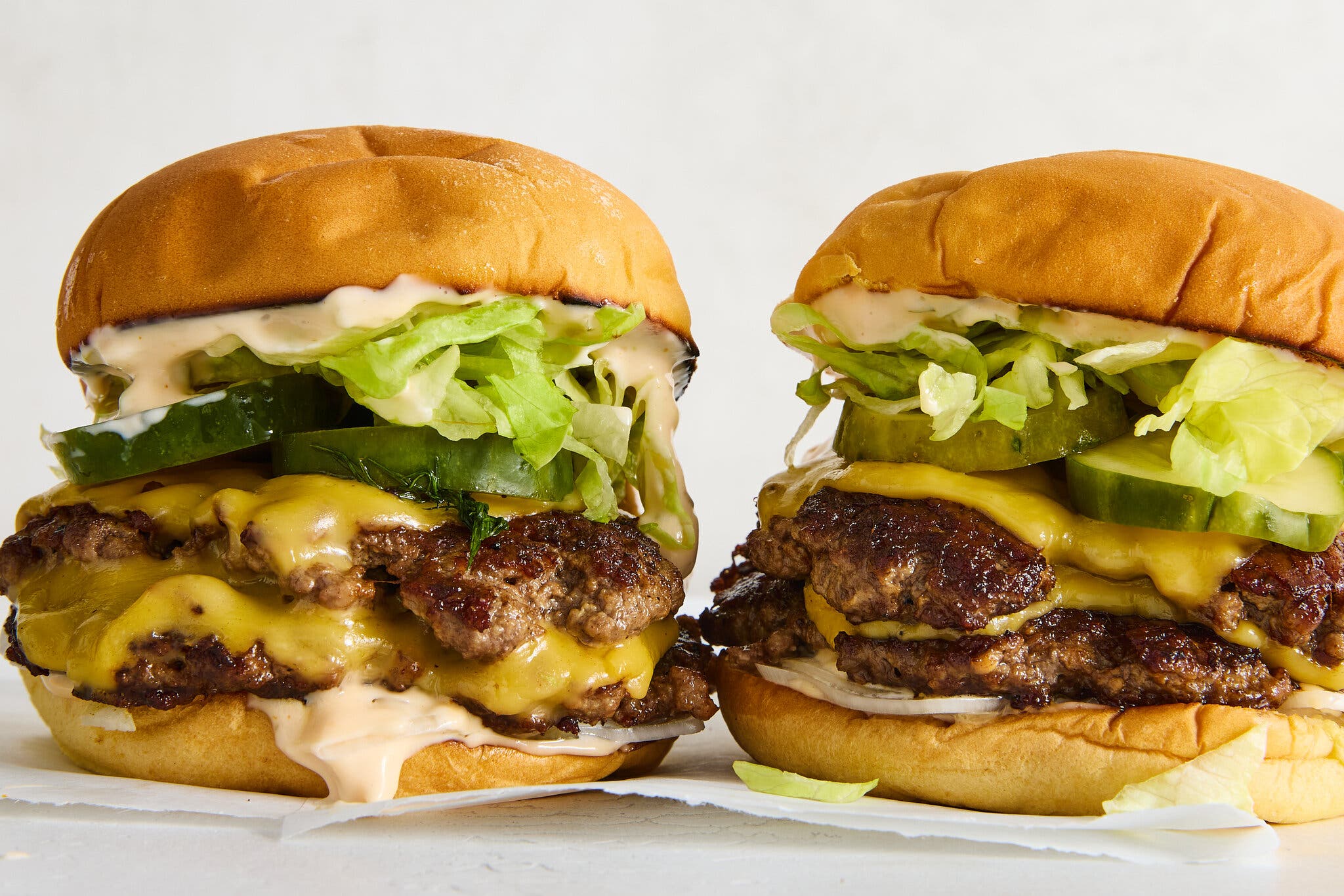 A side image of two smash burgers topped with lettuce, pickles and cheese.