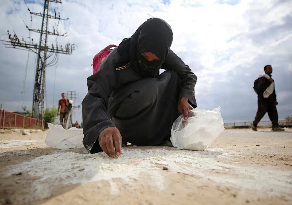 A woman collects flour from the ground as Palestinians receive aid supplies from the U.S.-backed Gaza Humanitarian Foundation (GHF) (Reuters)