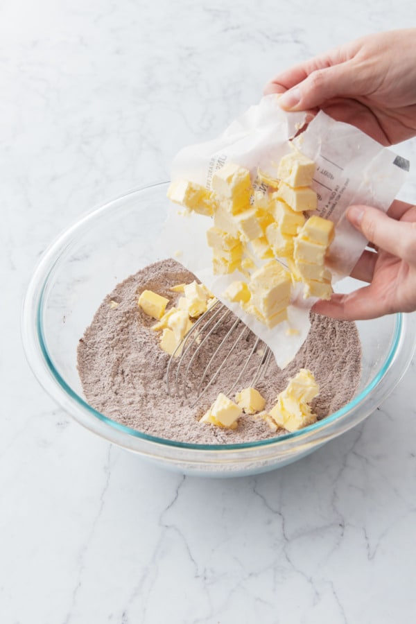Adding cubes of cold butter into mixing bowl with dry ingredients.