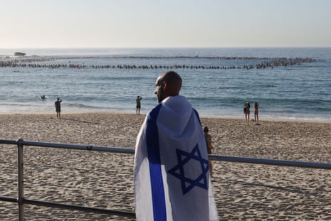 A man in an Israeli flag as the Bondi surfing community pays tribute to the victims of the mass shooting.